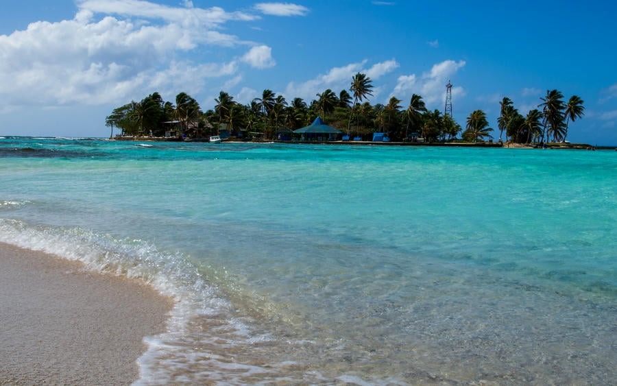Bellissima spiaggia chiara tropicale con mare cristallino. Sullo sfondo si vede un isolotto ricco di natura. 