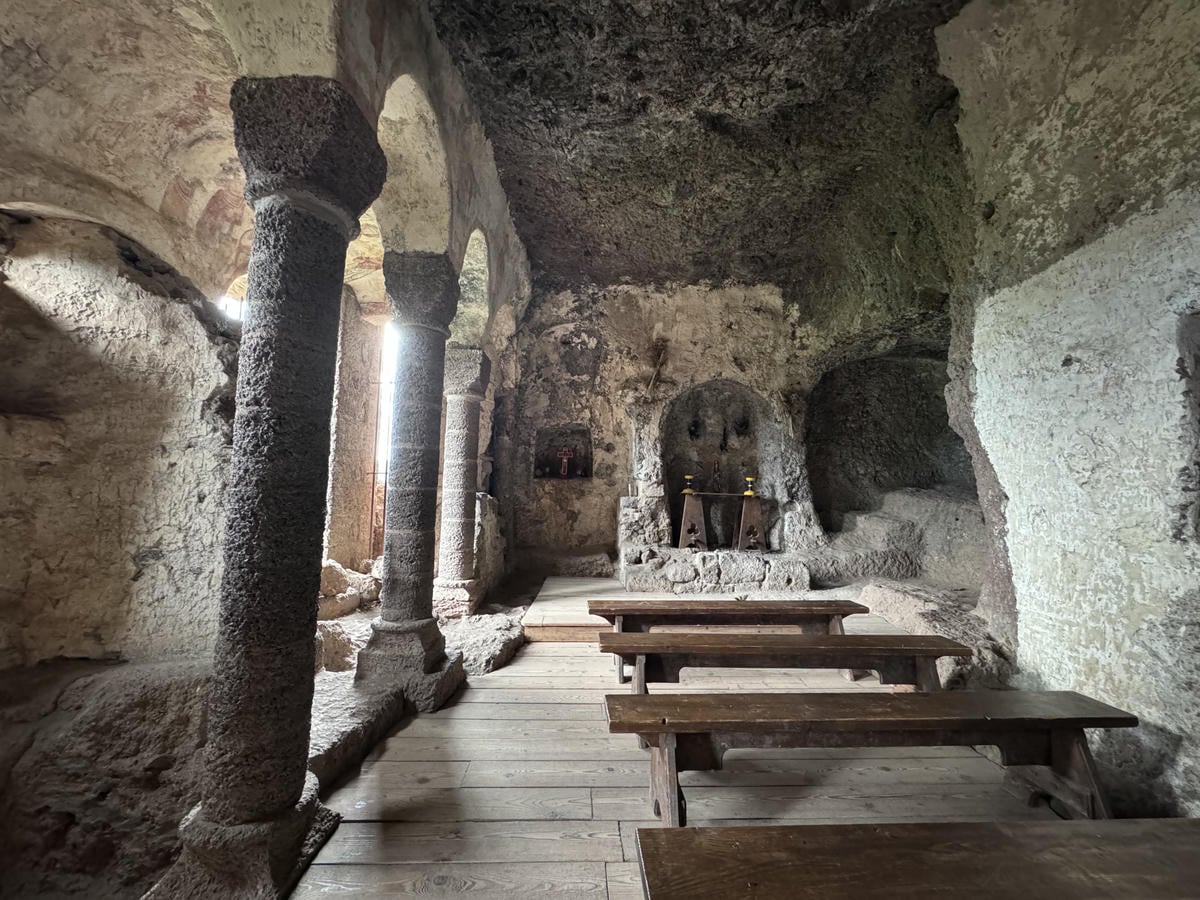 interno della cappella alle grotte di jonas. Presenza di colonne sulla sinistra, delle panche e in fondo un altare scavato nella roccia