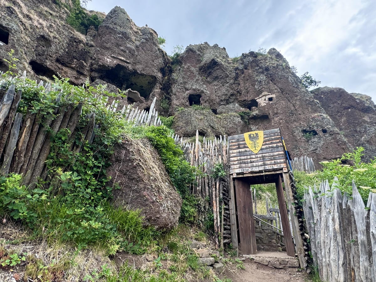 Entrata con una palizzata in legno, sullo sfondo una città scavata nella roccia vulcanica