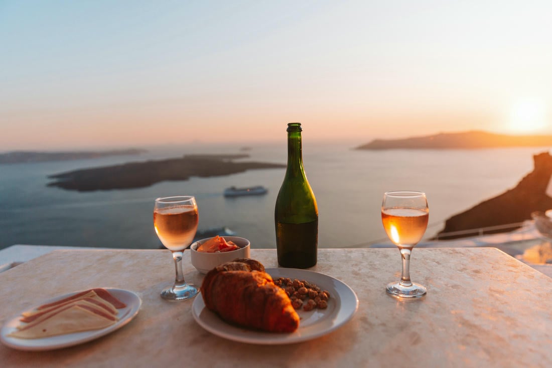 Un aperitivo a base di vino locale e stuzzichini su un balcone di Santorini, con vista sulla caldera all'ora del tramonto