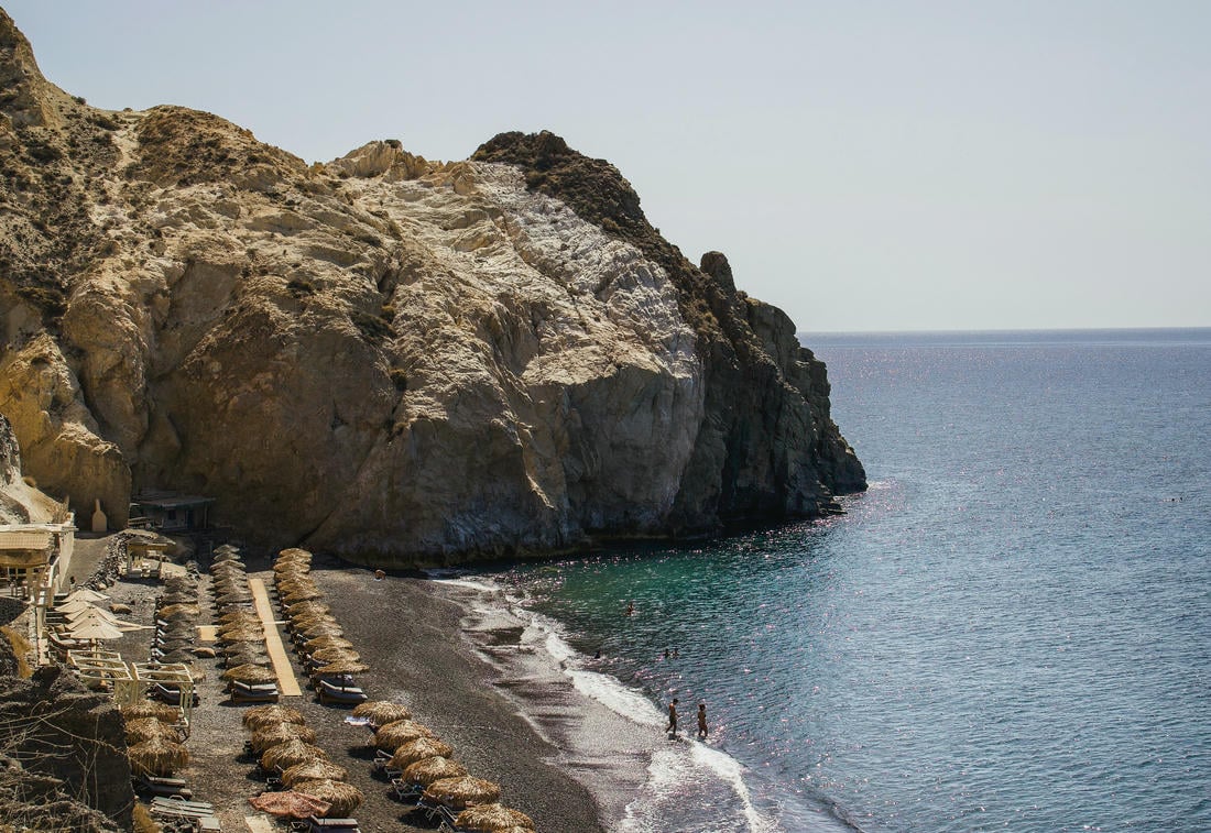 Spiaggia nera con lettini e ombrelloni a Santorini in Grecia