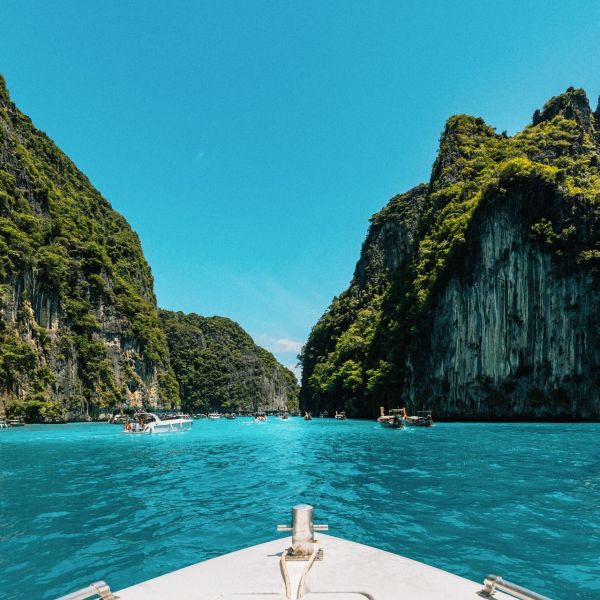 Prua di una barca che naviga un mare blu turchese, sullo sfondo dei faraglioni di roccia tipici della Thailandia